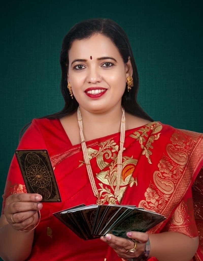 Dr. Abha Jain in a red silk saree, smiling and holding a fan of tarot cards